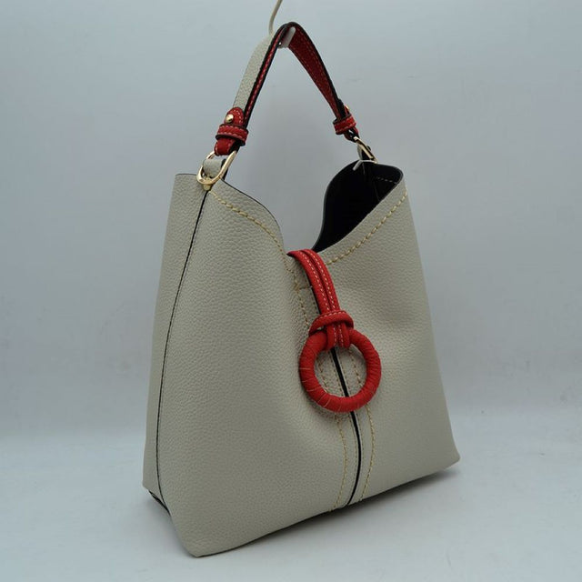 Beige This structured everyday bucket bag features a pebbled textured body with a distinctive curved, dip-top opening and prominent contrast stitching details along the front panel. It is designed with a singular flat top handle anchored to the sides by polished metal hardware loops for comfortable carrying. A central loop strap extends from the back to the front