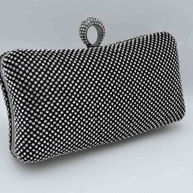 Black-silver This hard-shell box clutch features a curved rectangular profile entirely covered in neat rows of small, shimmering circular embellishments for an elegant accent to everyday ensembles. A prominent, textured ring-style clasp sits centered at the top, serving as both a functional closure mechanism to access the interior storage compartment and an integrated finger-loop handle element for secure hand-held carrying.