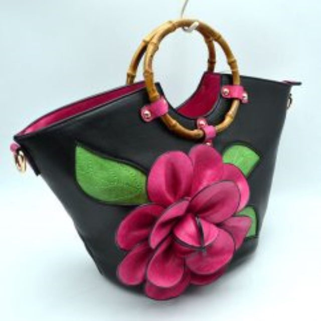 Black This structural tote bag is designed for standout everyday use, showcasing a prominent three-dimensional floral applique paired with stitched leaf accents on the front panel. It features segmented, circular top handles secured to the curved upper rim with studded contrasting tabs. The main storage compartment opens widely at the top to reveal a vibrant interior lining