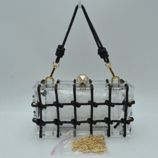 Black This unique everyday box clutch bag features a transparent structured body enclosed in a distinctive knotted cage overlay. Designed for specialized daily or evening use, the main storage compartment is secured by a top frame with a geometric metallic clasp closure. It offers versatile carrying options, equipped with a flexible cord top handle attached to the top panels via polished metal loops, alongside a separate metallic chain strap included at the base.