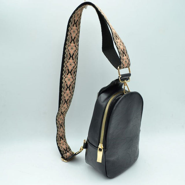 Black This compact sling backpack features a smooth textured finish and a contoured, teardrop-shaped silhouette designed for casual everyday use. It includes a primary storage compartment that secures with a prominent gold-tone zipper and a flat pull tab for easy access to essentials. A distinctive, wide shoulder strap decorated with an intricate geometric pattern connects via gold-tone metal clips to various anchor loops, allowing for adjustable and versatile cross-body or over-the-shoulder wear.