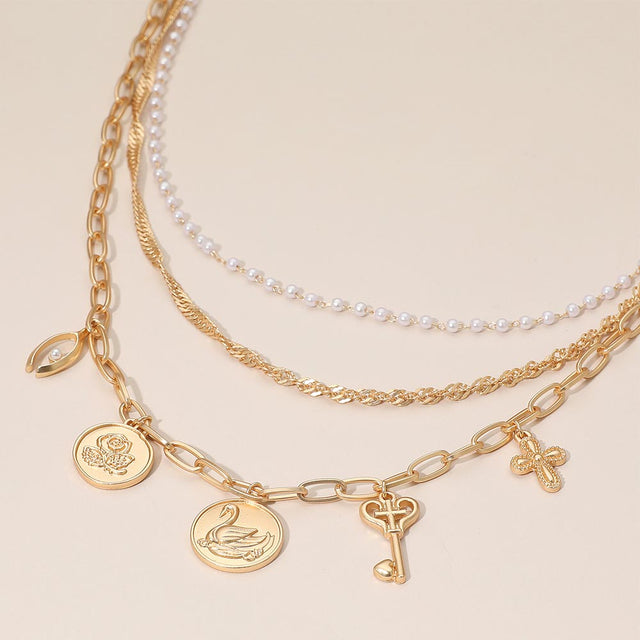 Madeline Love Cream, Matte gold Flower Swan Embossed Medallion Key Cross Pearl Charm Station Layered Chain Necklace - Necklaces