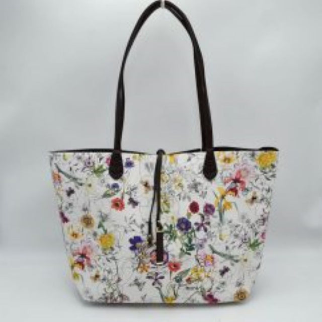Flora This everyday tote bag features an all-over vibrant floral and botanical pattern across its spacious main compartment. Designed for daily use, it is equipped with slim double shoulder straps attached securely to the front and back panels. A central decorative thin tie closure accents the open top design, completing the sleek and functional look.