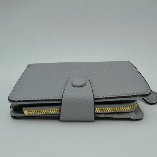 Gray This compact everyday wallet features a distinct pebbled texture and neat border stitching for a clean, structured appearance. Designed for efficient organization, the multi-compartment layout includes an accessible side storage compartment with a metallic zipper alongside a fold-over section secured by a central strap and snap-button closure. Its streamlined profile easily slips into larger bags or can be carried independently