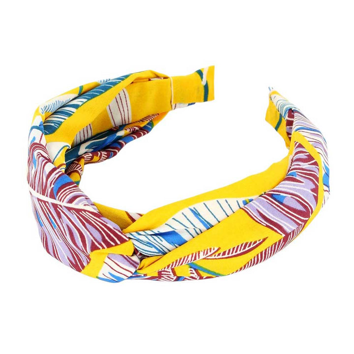 Mustard Tropical Leaf Patterned Twisted Headband, perfect for adding a touch of summer to any outfit. Crafted with a unique twisted design and featuring a vibrant tropical leaf pattern, this headband is both stylish and functional. Stay on-trend and keep your hair in place with this fashionable accessory.