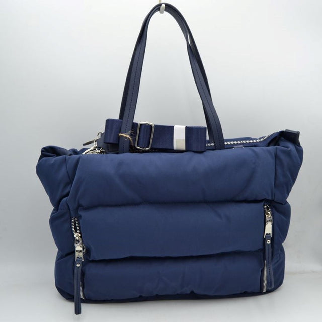 Navy This functional tote bag features a soft, insulated puffer exterior with horizontal quilted channels in a sleek deep navy blue, making it an excellent choice for casual everyday use or travel. Designed for efficient organization, the front is equipped with two vertical side-entry zipper pockets with long fabric pulls for quick access to smaller items. It comes with sturdy flat dual top handles for a comfortable shoulder carry